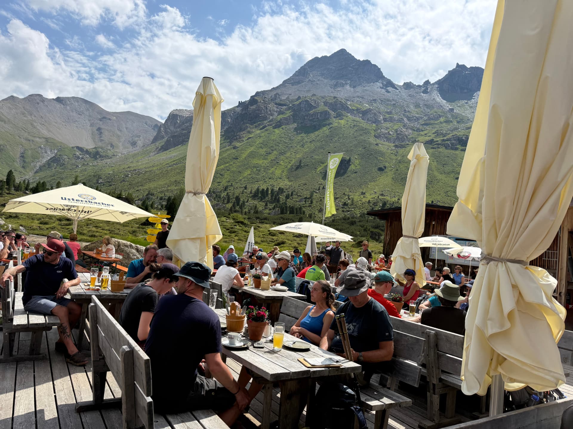 Gut besetzte Sonnenterrasse der Lizumer Hütte mit Gästen an Holztischen, dahinter die Bergkulisse der Lizum.