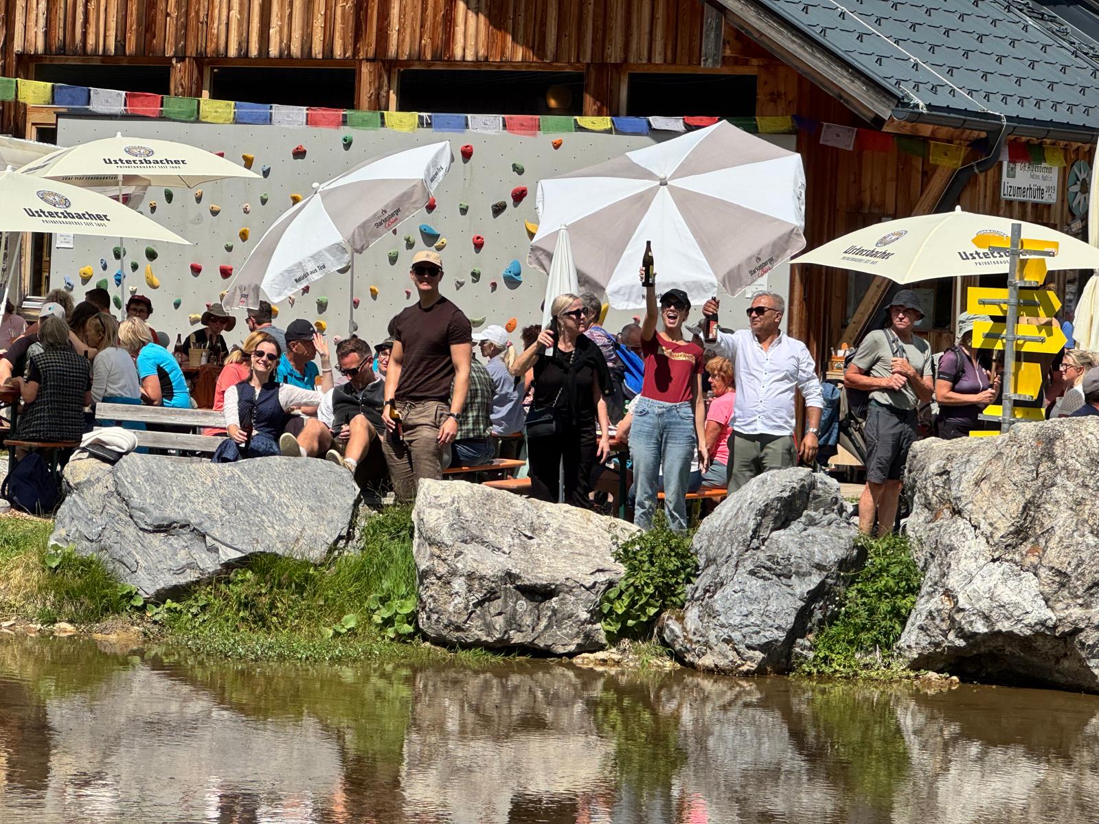 Besucherinnen und Besucher stehen und sitzen am Teich vor der Lizumer Hütte, geschmückt mit Wimpelketten.
