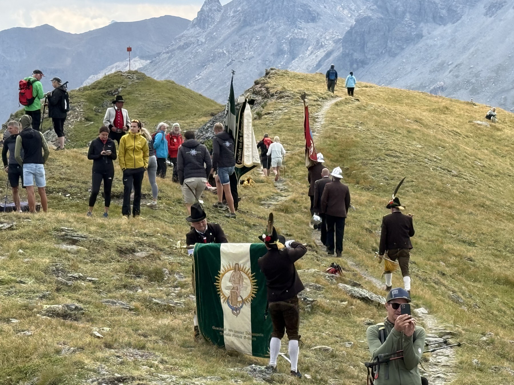 Schützen und Fahnenabordnungen mit Vereinsfahnen ziehen über den Bergrücken zur Mölsbergmesse.