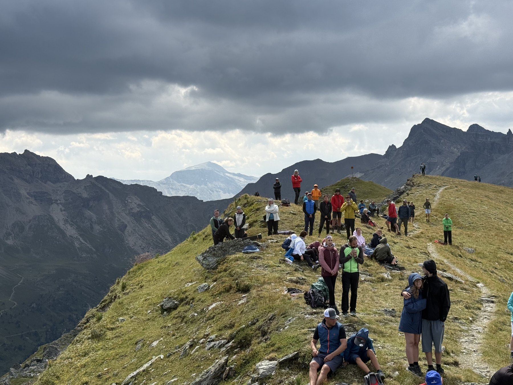 Besucherinnen und Besucher verteilen sich am Grat, im Hintergrund Wolken und Gletscherblick.