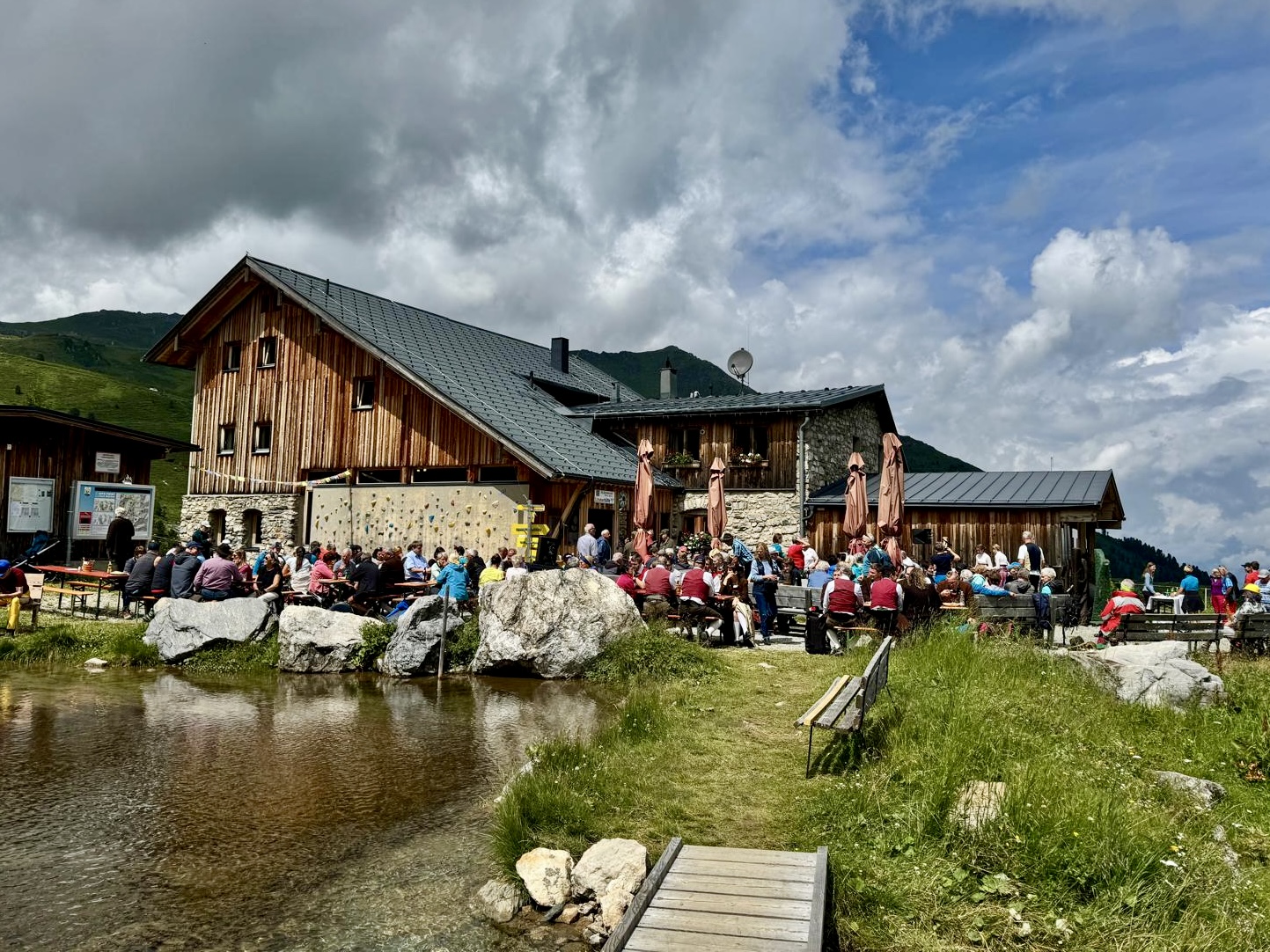 Lizumer Hütte im Sommer mit zahlreichen Gästen auf der Terrasse und am Wiesenbach – Musikantentreffen 2025.