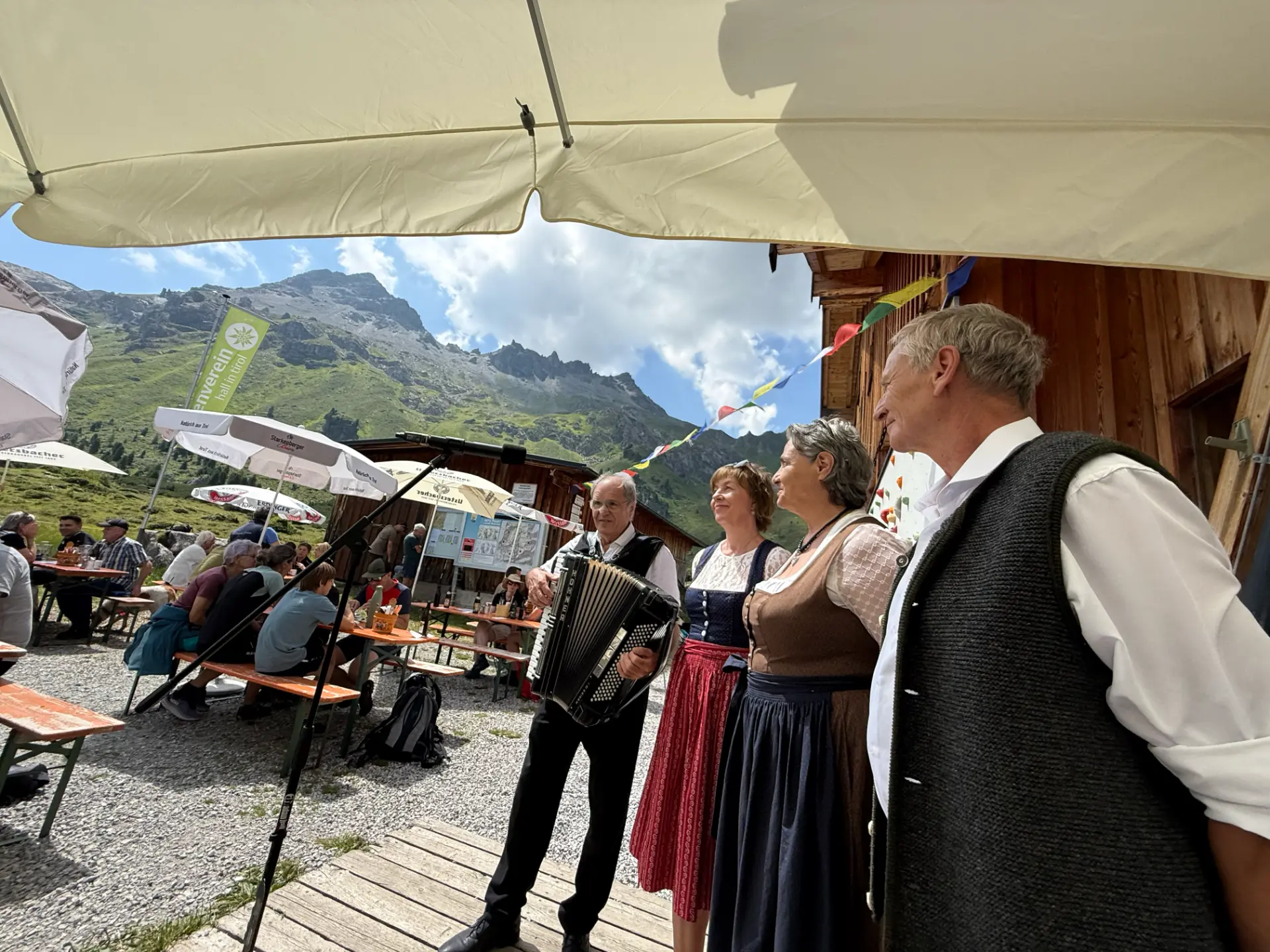 Musikanten in Tracht mit Ziehharmonika vor der Lizumer Hütte, im Hintergrund Bergkulisse und Gäste an den Tischen.