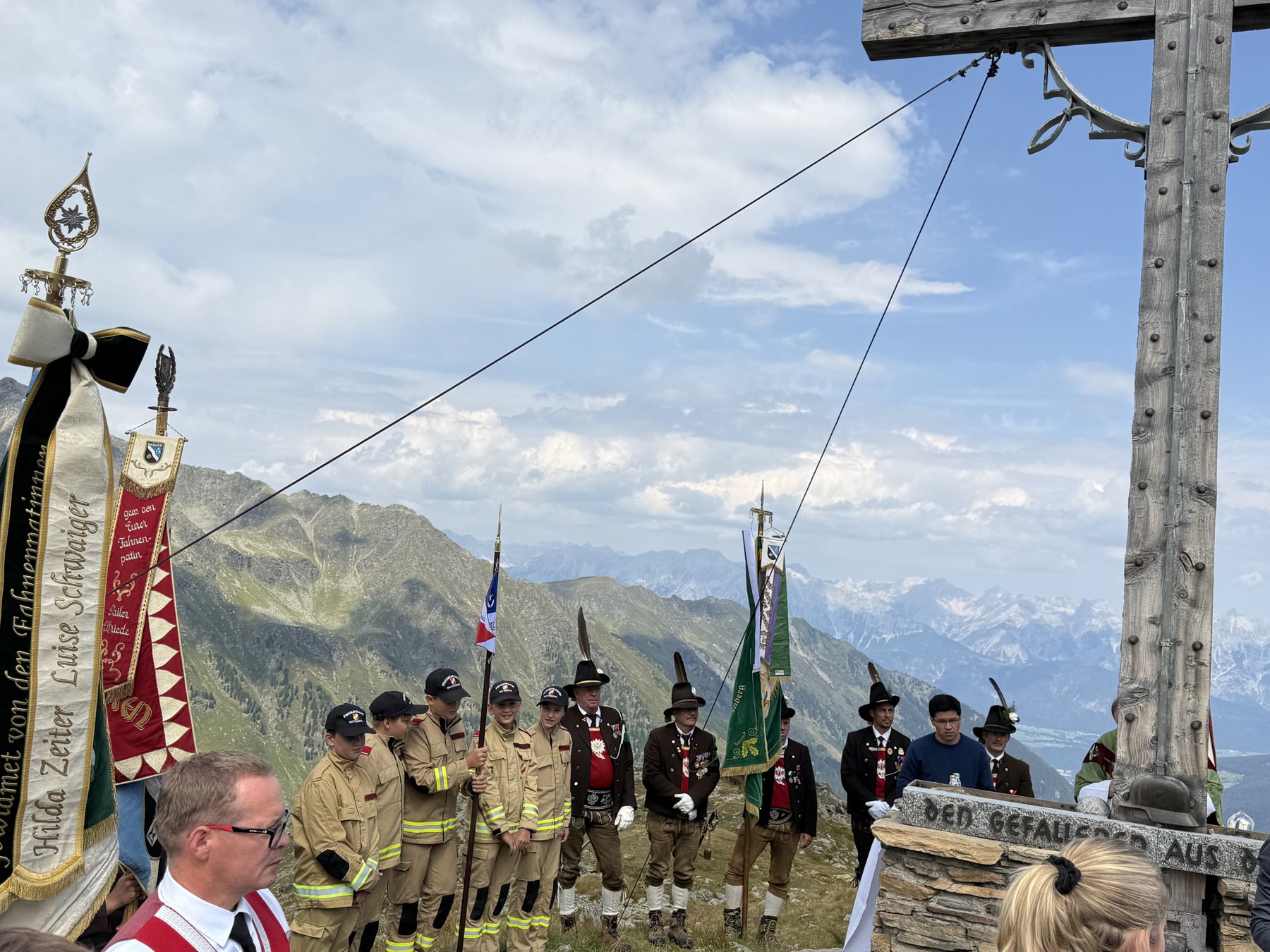 Feuerwehrjugend, Schützen und Fahnenabordnungen stehen beim Gipfelkreuz Spalier.