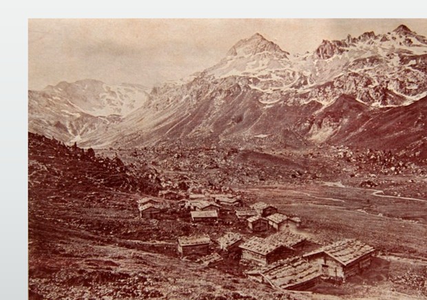 Historische Sepia-Aufnahme der Alpe Lizum um 1920: verstreute Almhütten im weitläufigen Talboden, umrahmt von schroffen, schneebedeckten Gipfeln.