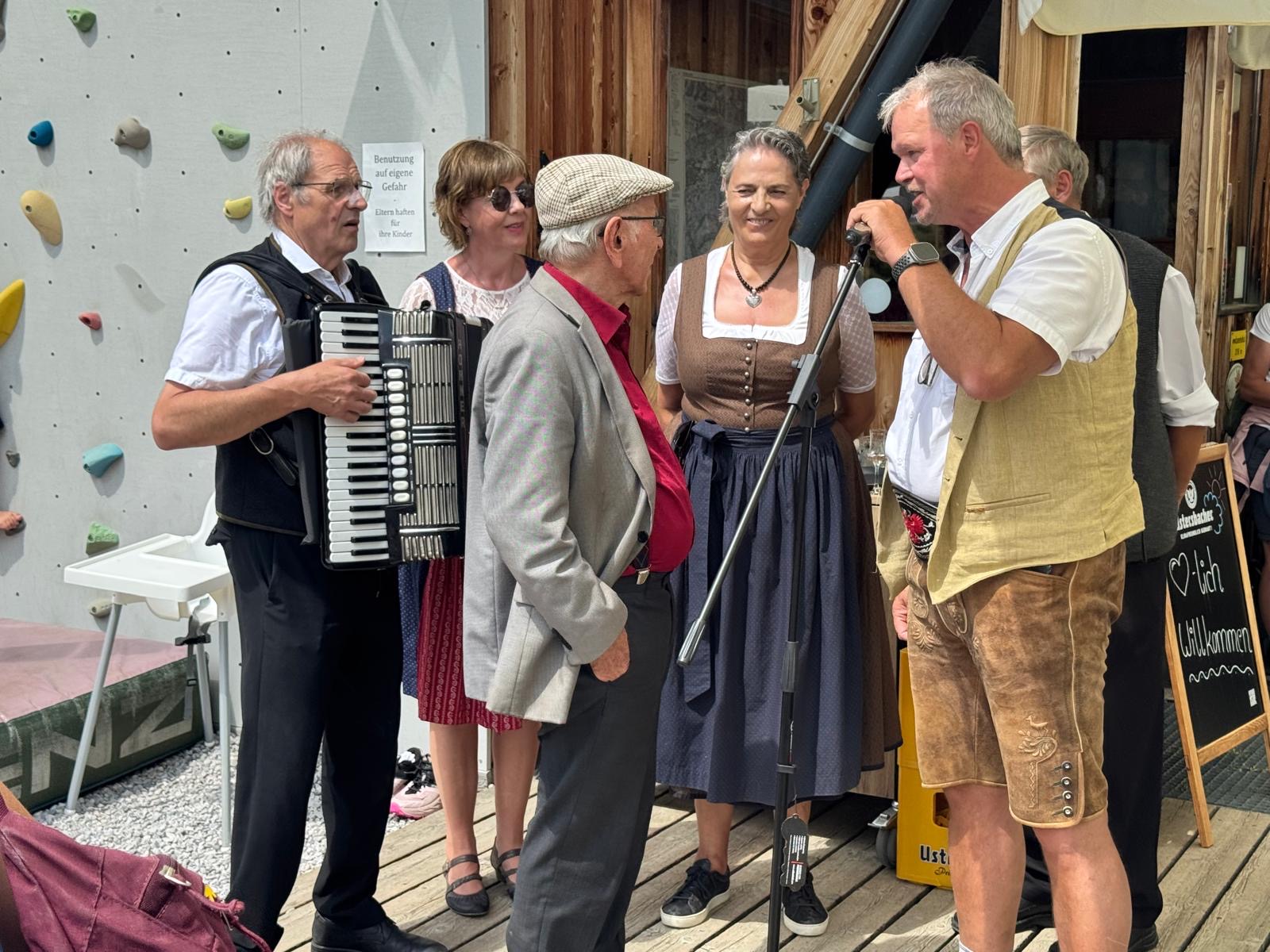 Musikantinnen und Musikanten in Tracht singen und musizieren am Mikrofon bei der Lizumer Hütte.
