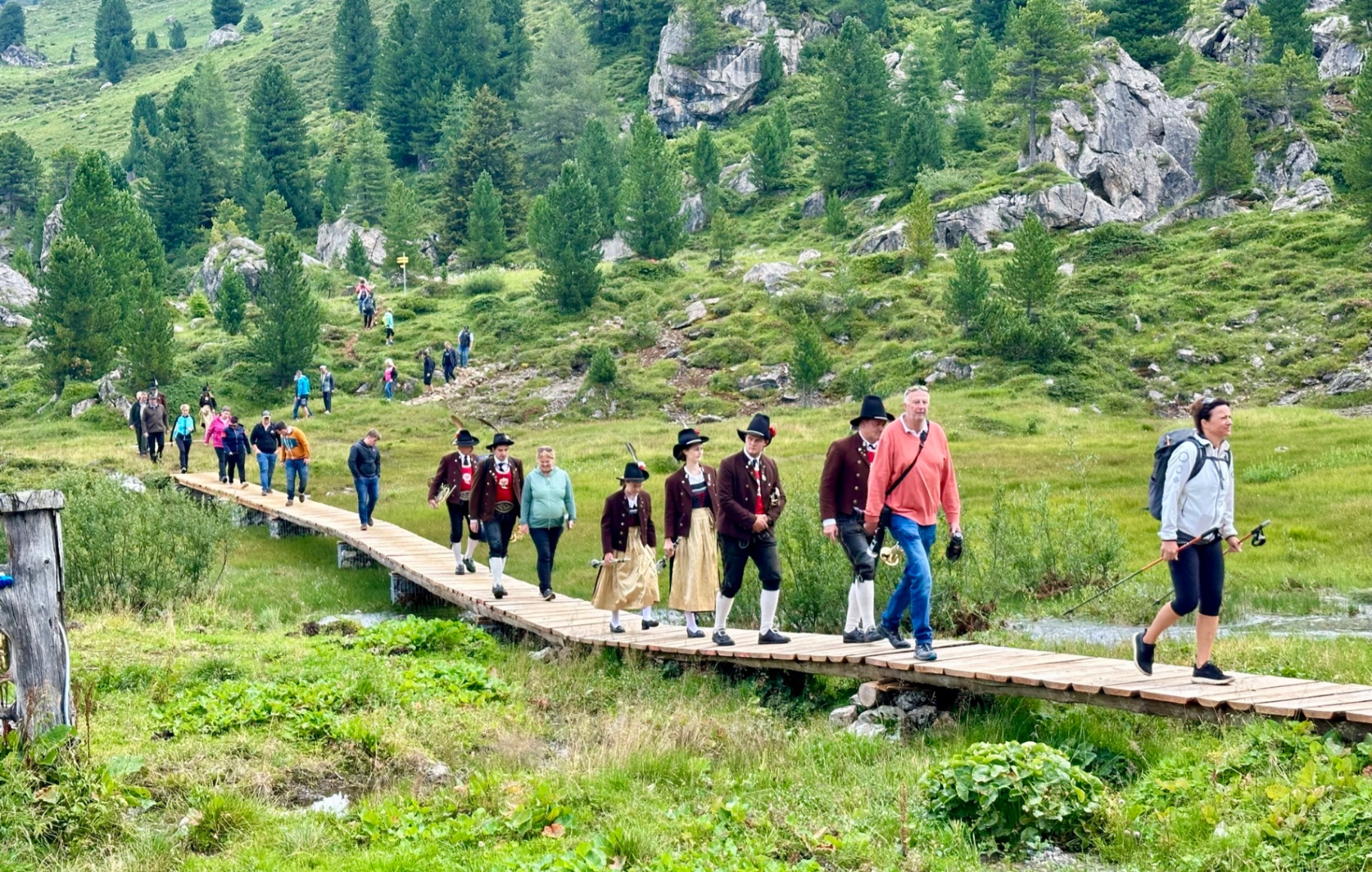 Wandergruppe und Menschen in Tracht überqueren einen Holzsteg im Wattental – Brücken verbinden Wege und Menschen